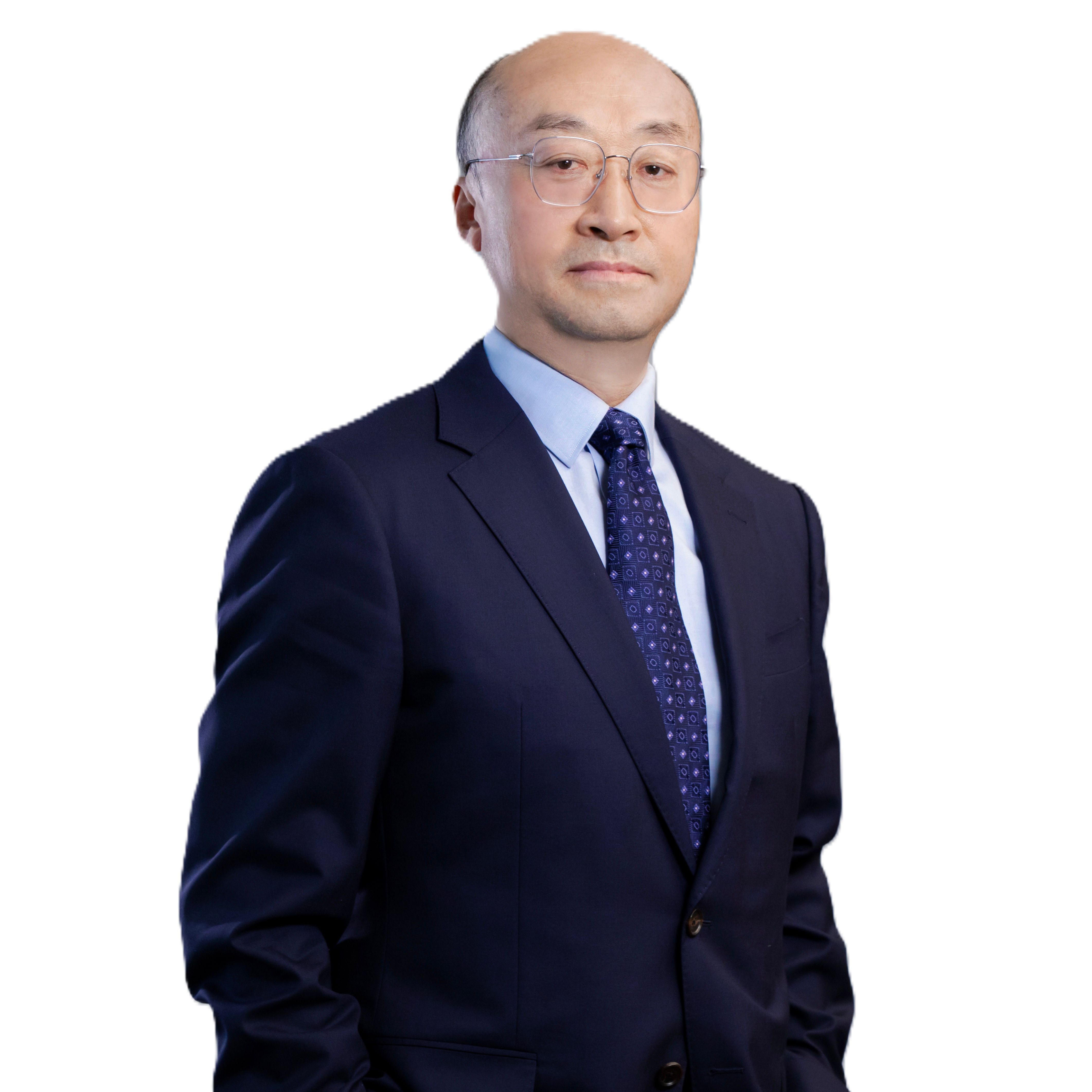 Bald Asian man in a dark suit and blue patterned tie looking forward.