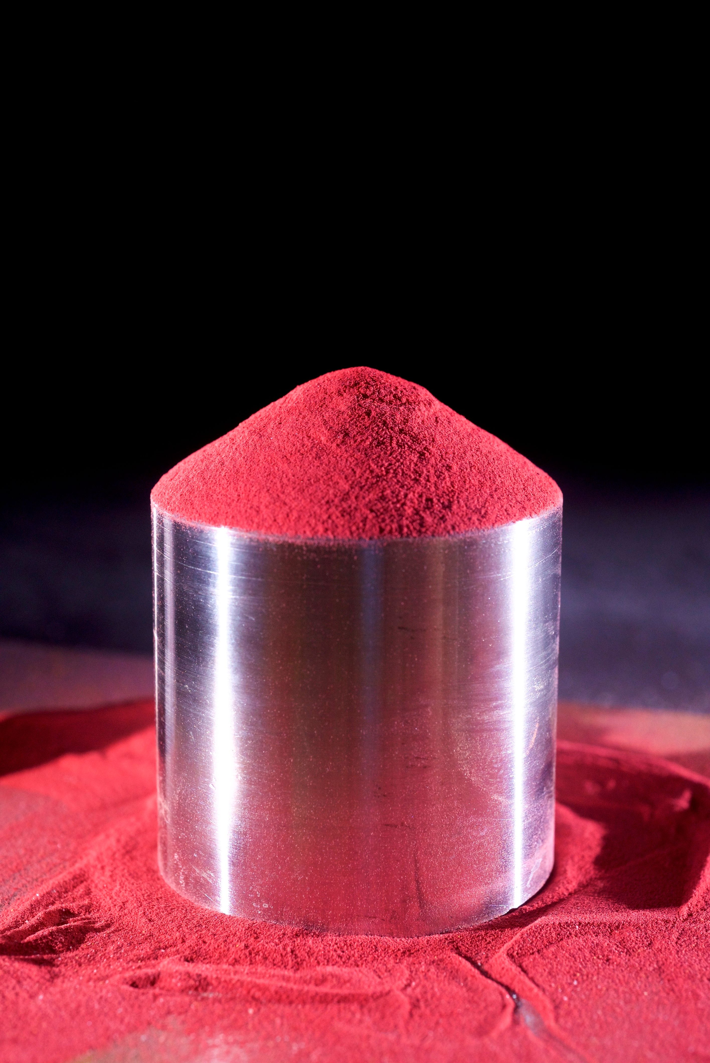 A silver cylindrical container holds vibrant red powder mounded into a cone shape.