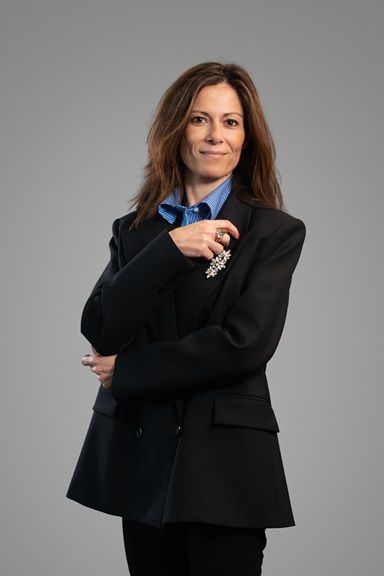 Professional woman with long brown hair in a dark blazer and blue shirt.
