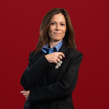 Une femme vêtue d'un tailleur sombre et d'une chemise bleue tient une broche en argent.
