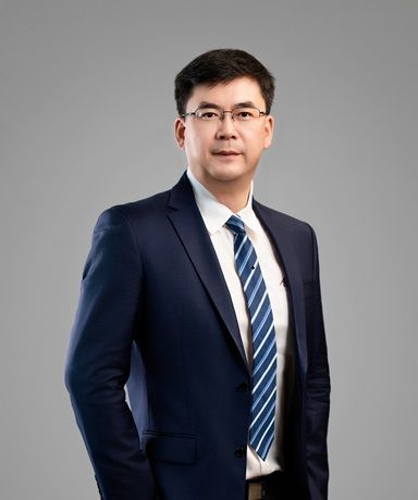 Professional man in a dark suit, white shirt, and striped tie, wearing glasses.