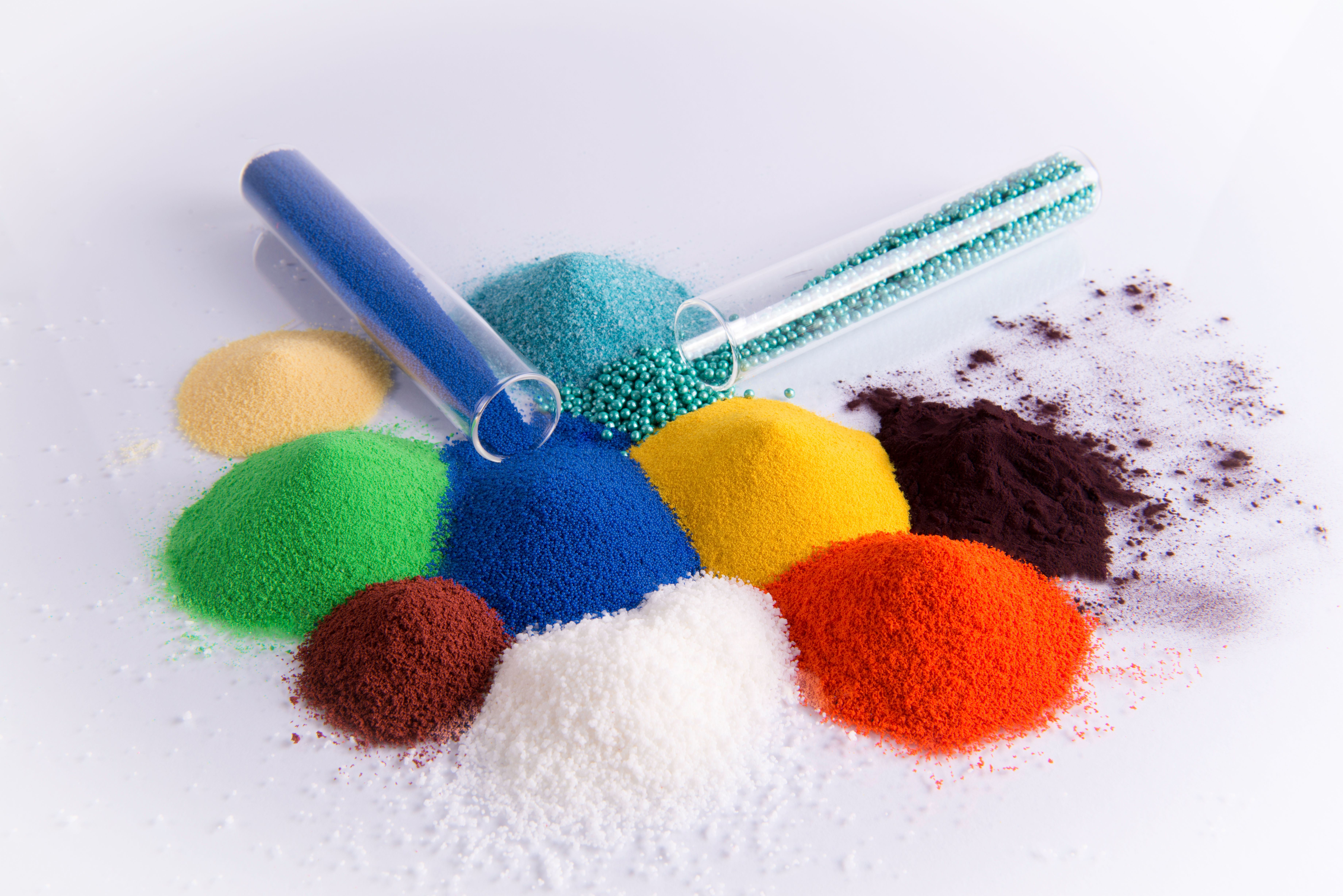 Piles of colorful chemical powders in various hues, with a blue test tube and brush.