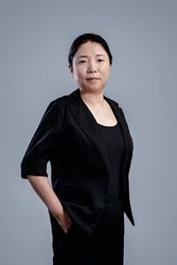 East Asian woman in black jacket stands with hands in pockets.