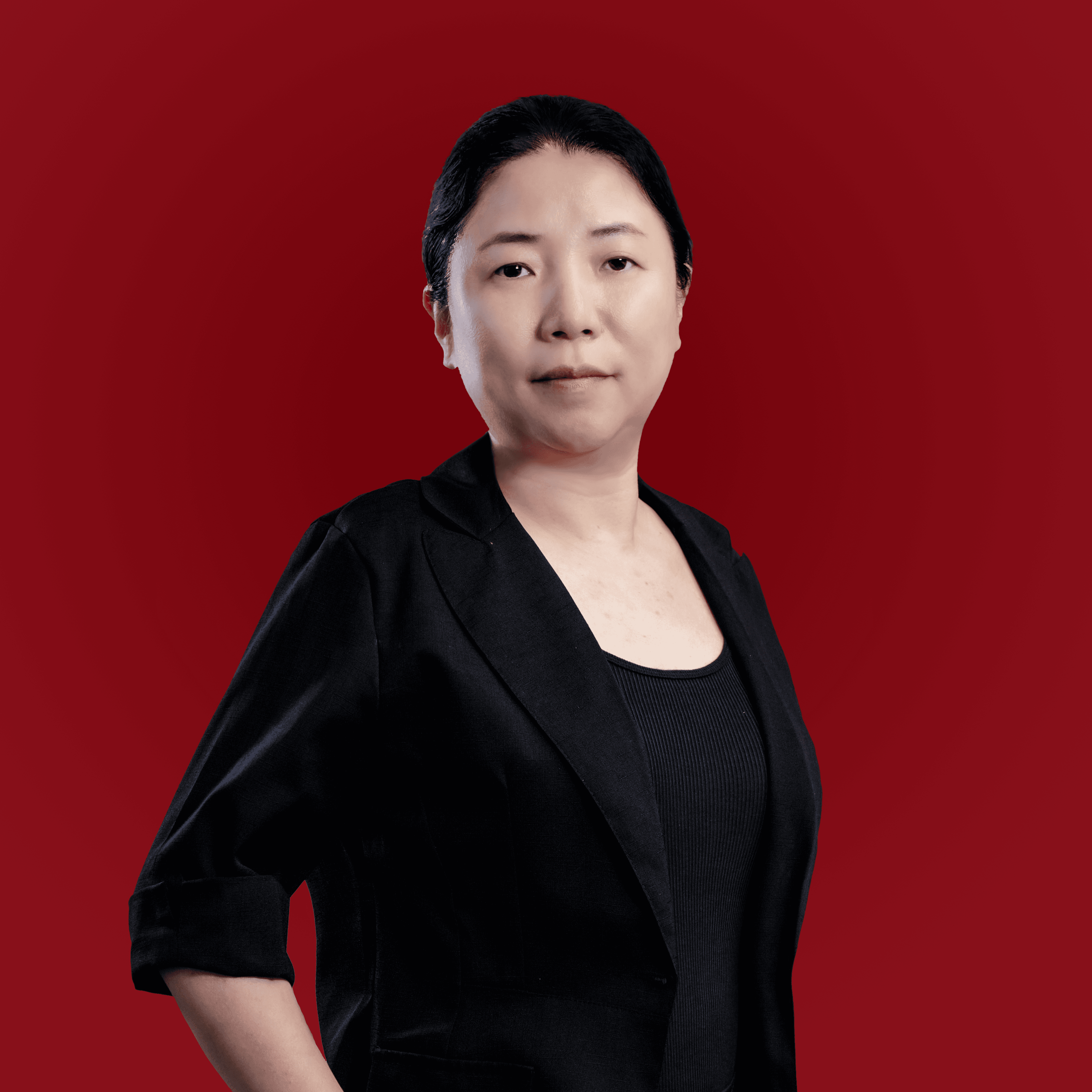 Une femme asiatique en tenue professionnelle, vêtue d'un blazer noir, se tient, l'air assuré, devant un fond rouge.