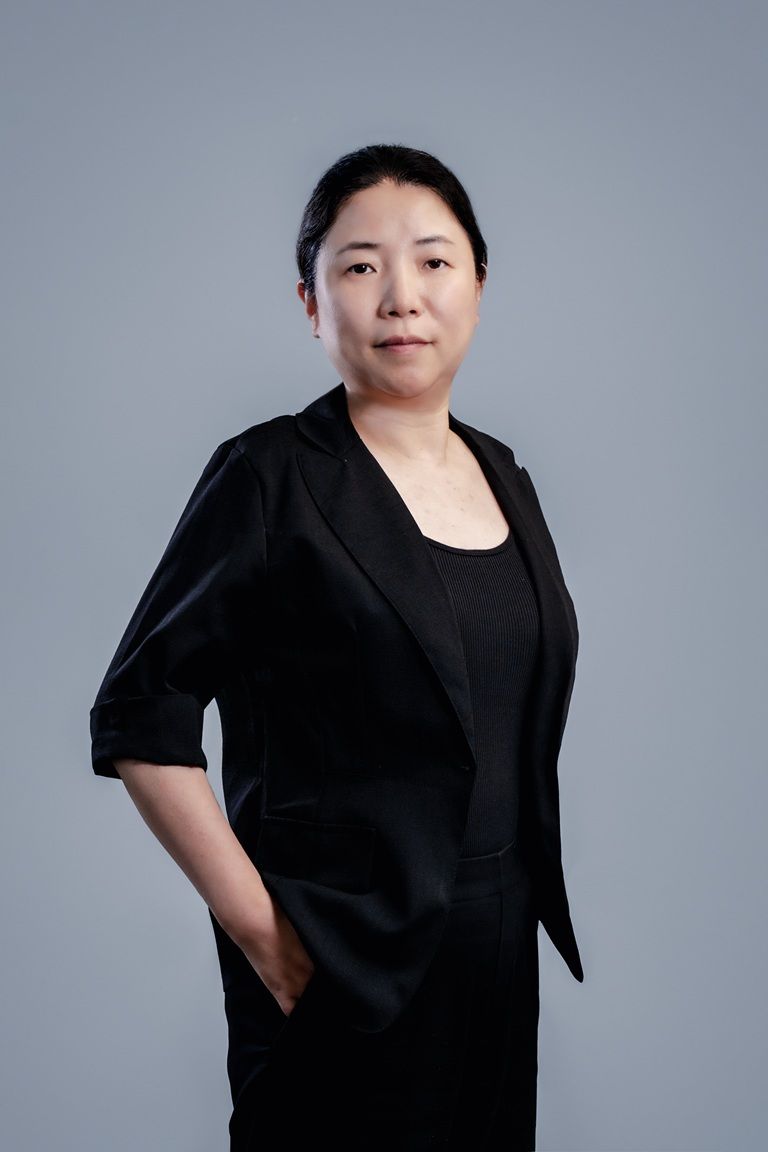 一位身穿黑色西装外套的亚洲女性自信地站立着，目光直视观众。