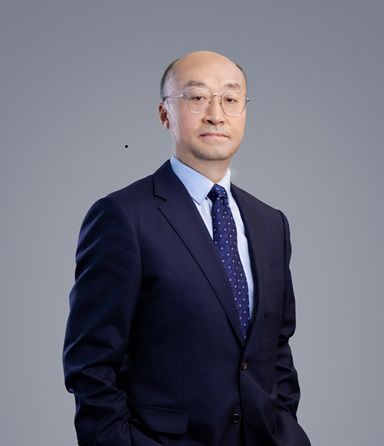 A professional Asian man in a dark suit and glasses looks directly ahead.