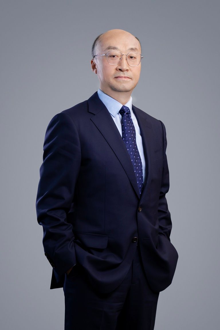 一名身穿深色西装、系着蓝色领带的男子双手插在口袋里站着。